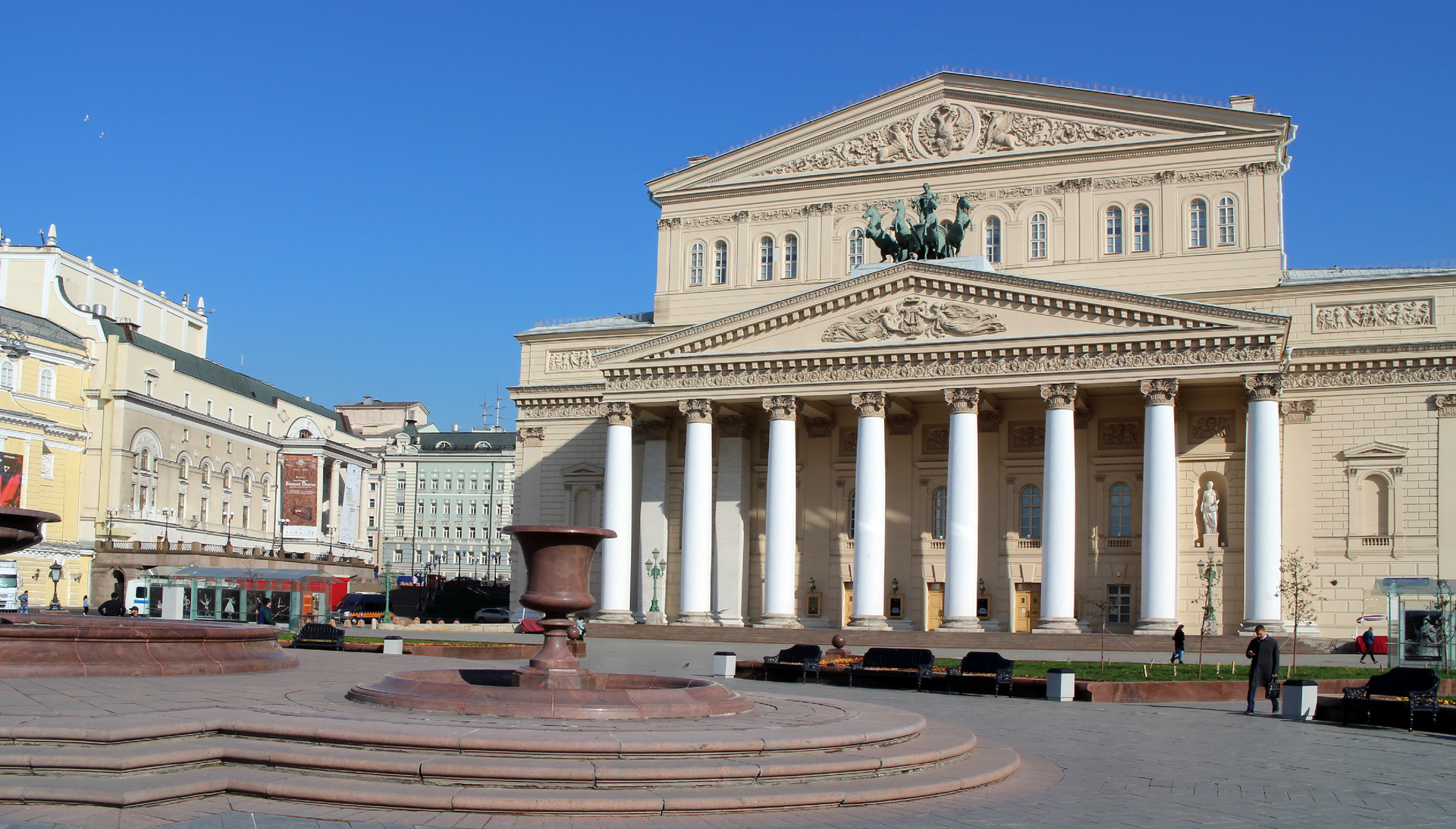 Ilustracja przedstawia neoklasycystyczny budynek teatru w Moskwie. Przed budynkiem widoczny jest spory plac.