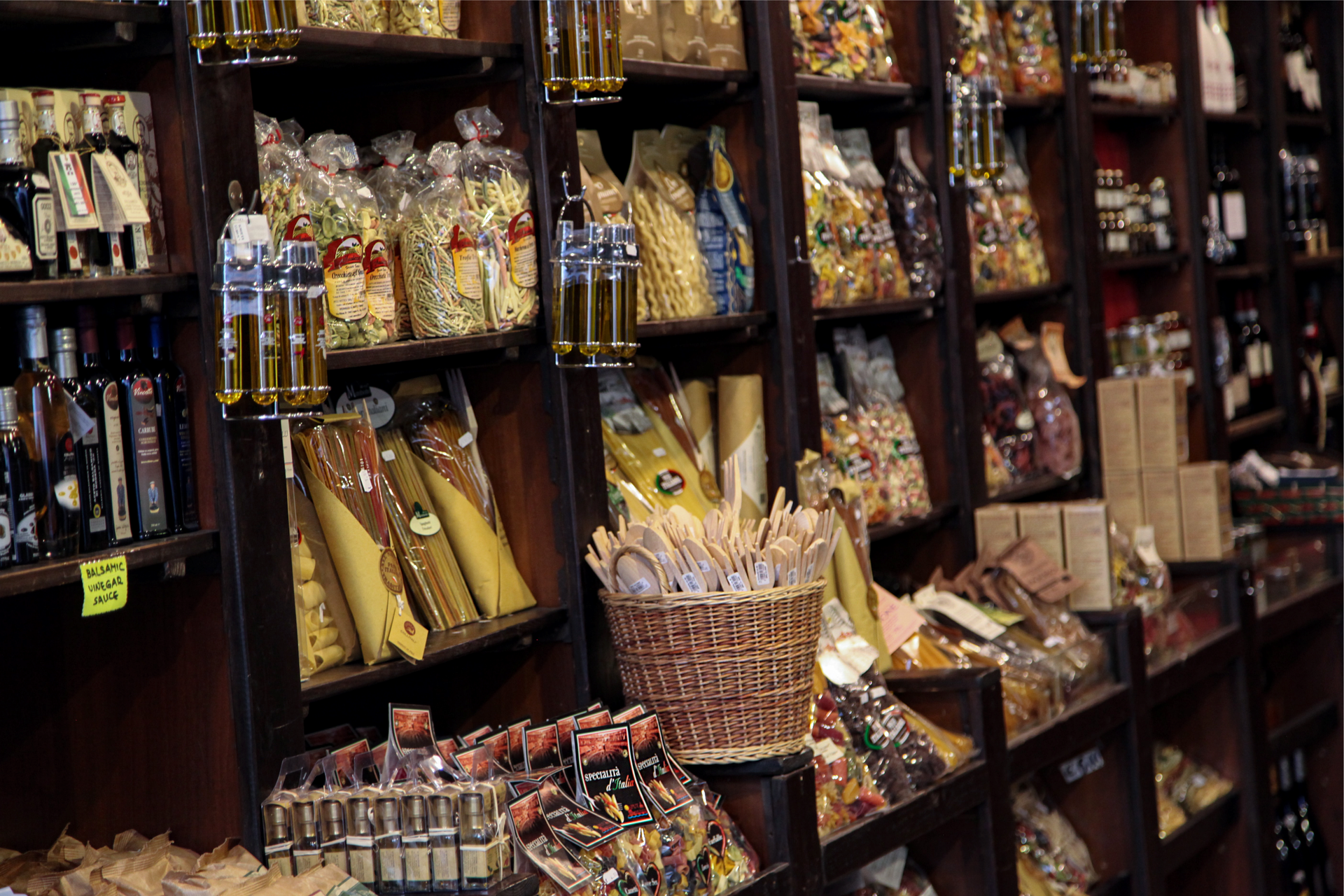 Zdjęcie przedstawia regał z półkami w sklepie z włoskimi produktami spożywczymi. Na półkach widać różnego rodzaju makarony, butelki z oliwą.