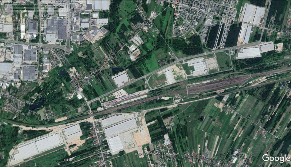 Fotografia lotnicza przedstawia Łódź Olechów – centrum logistyczne i dystrybucyjne (Panattoni Park Łódź East) oraz stację kolejową. W centrum znajduje się droga biegnącą przez środek terenu, od której odchodzą boczne ulice. Na zdjęciu widać również pola i lasy w różnych odcieniach zieleni oraz białe prostokąty, które są dachami budynków przemysłowych.