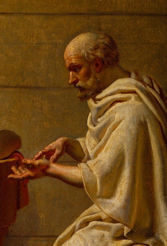 Fragment obrazu malarskiego przedstawiającego postać Sokratesa przemawiającego do swojego ucznia. Jest to starszy mężczyzna o ostrych rysach twarzy. Z przodu jego głowy widać wyraźną łysinę, z tyłu kręcone włosy opadające na szyję. Mężczyzna ubrany jest w długą zwiewną szatę przerzuconą przez lewe ramię. Z przodu na wysokości klatki piersiowej trzyma dłonie. Prawą dłonią dotyka lewej dłoni.