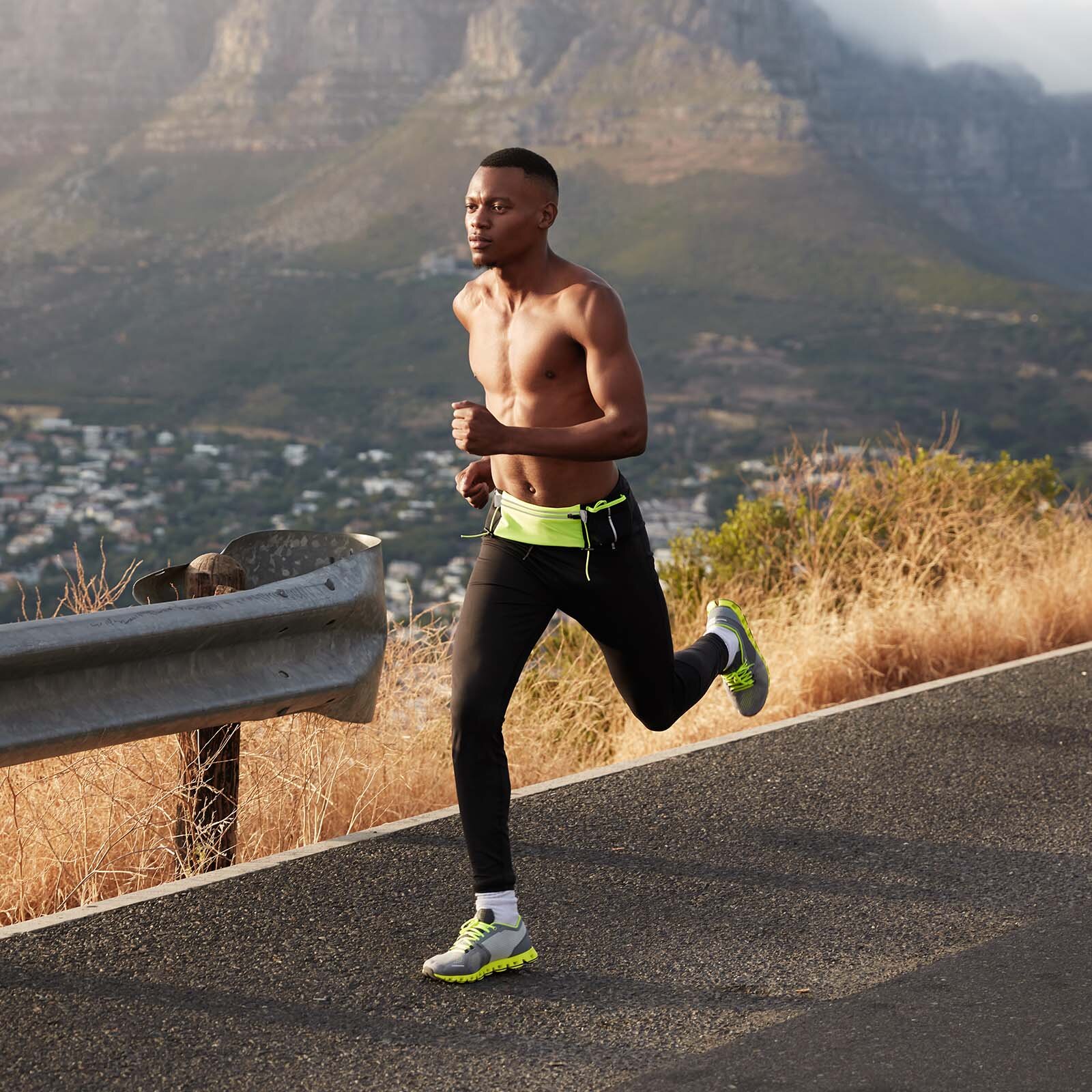 Zdjęcie przedstawia mężczyznę biegnącego po asfalcie. Mężczyzna ma na sobie legginsy oraz buty do biegania. Biegnie bez koszulki. 
