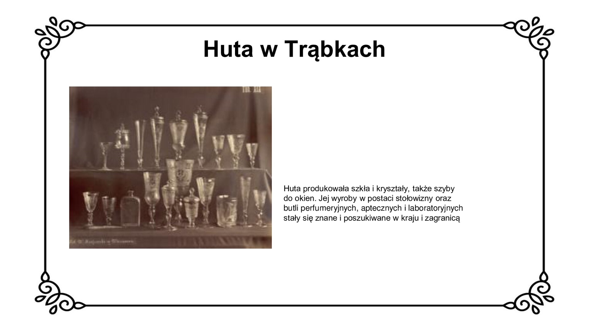 Biały slajd. U góry nagłówek: „Huta w Trąbkach”. Poniżej, z lewej strony slajdu, czarno‑białe zdjęcie szkła garwolińskiego. Na dwóch poziomach prezentacji ustawiono szklane kieliszki, kielichy, szklanki, butelki na wódkę i puchary. Obok zdjęcia, z prawej strony slajdu, tekst: „Huta produkowała szkła i kryształy, także szyby do okien. Jej wyroby w postaci stołowizny oraz butli perfumeryjnych, aptecznych i laboratoryjnych stały się znane i poszukiwane w kraju i zagranicą”.