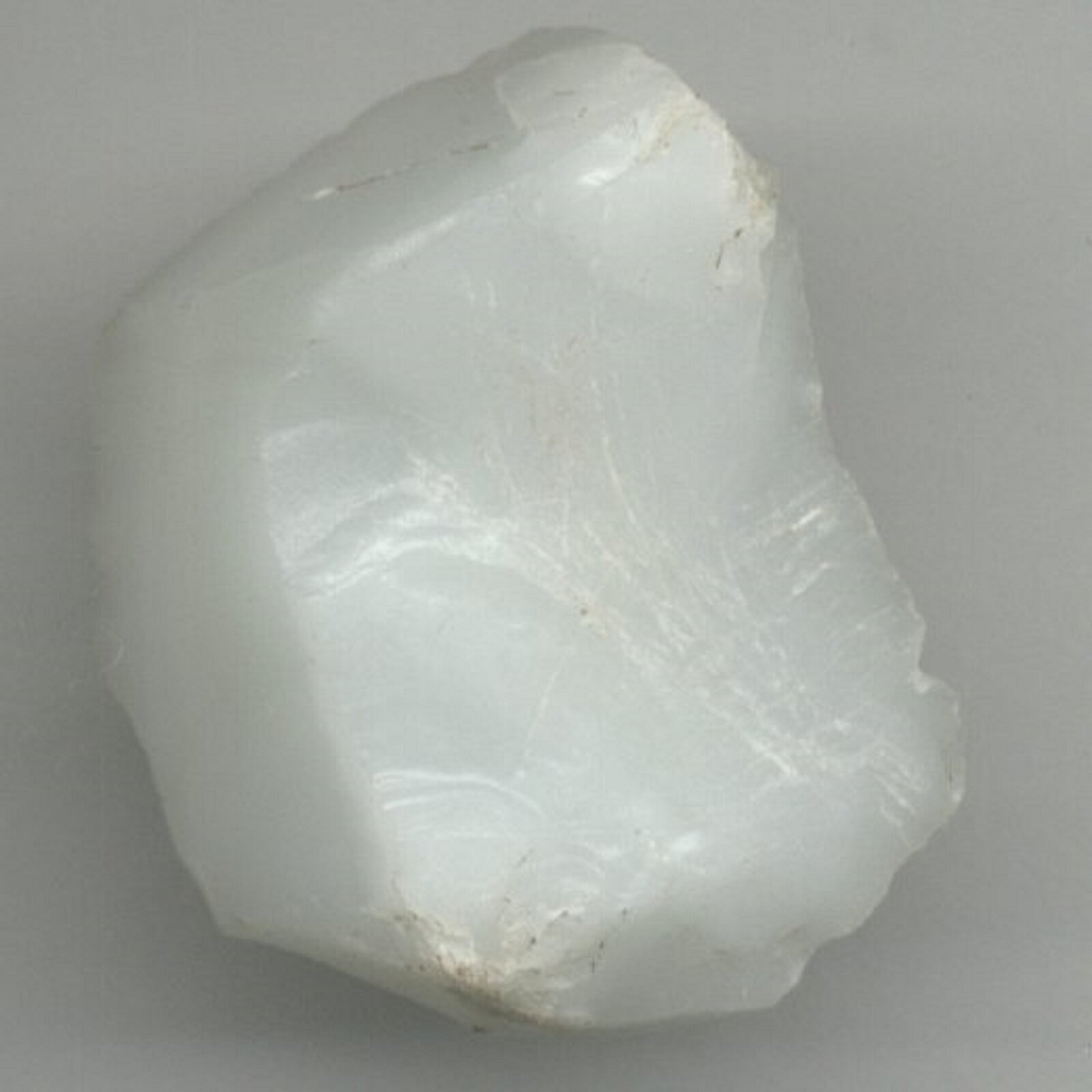 Ilustracja przedstawia kryształ kwarcu mlecznego. Kamień ma biały kolor, jego powierzchnia jest gładka i niematowa.