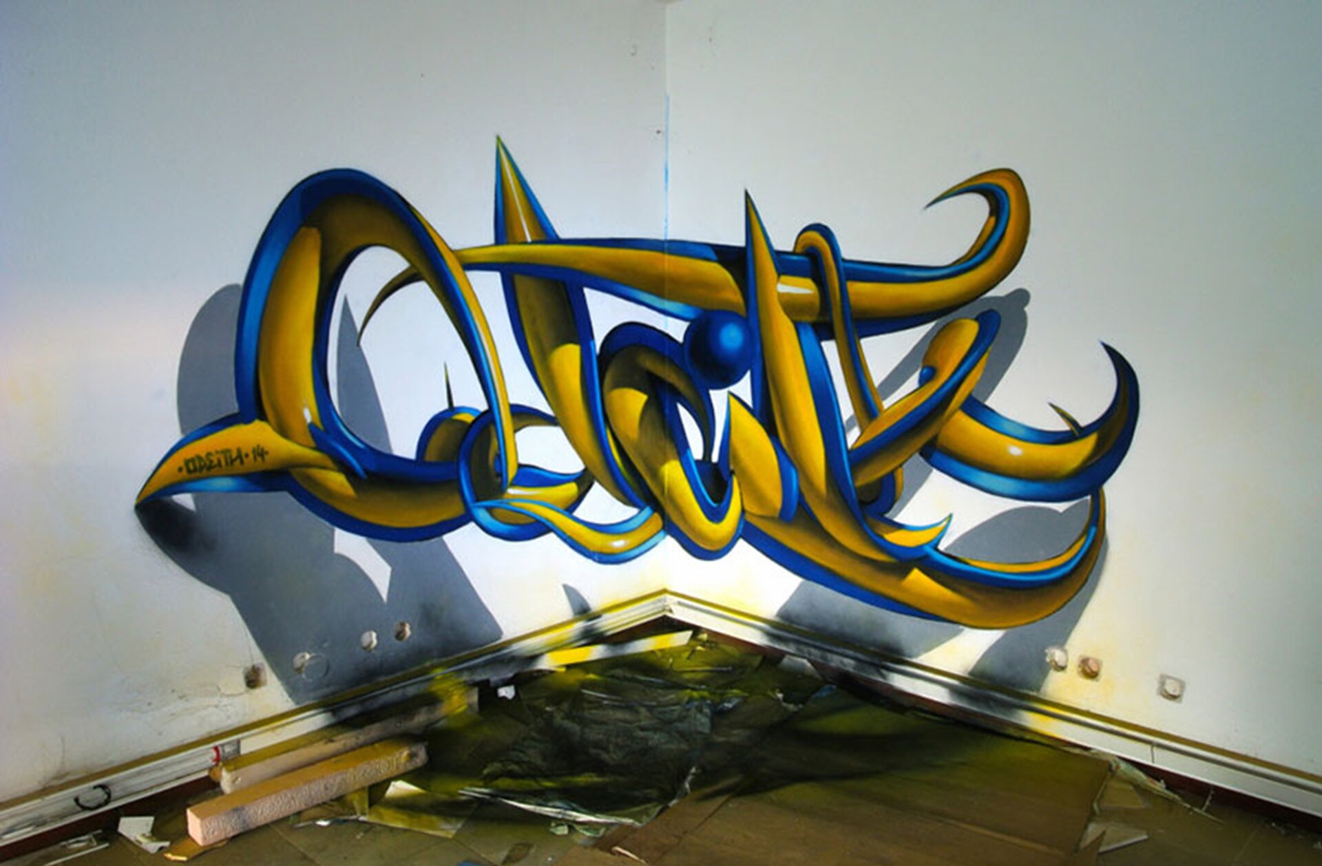 Ilustracja przedstawia graffiti Sergio Odeith'a. Ukazuje żółty napis z niebieskim konturem zamieszczony w rogu ściany w taki sposób, że tworzy efekt trójwymiarowy. Na ścianie i podłodze został namalowany cień napisu.