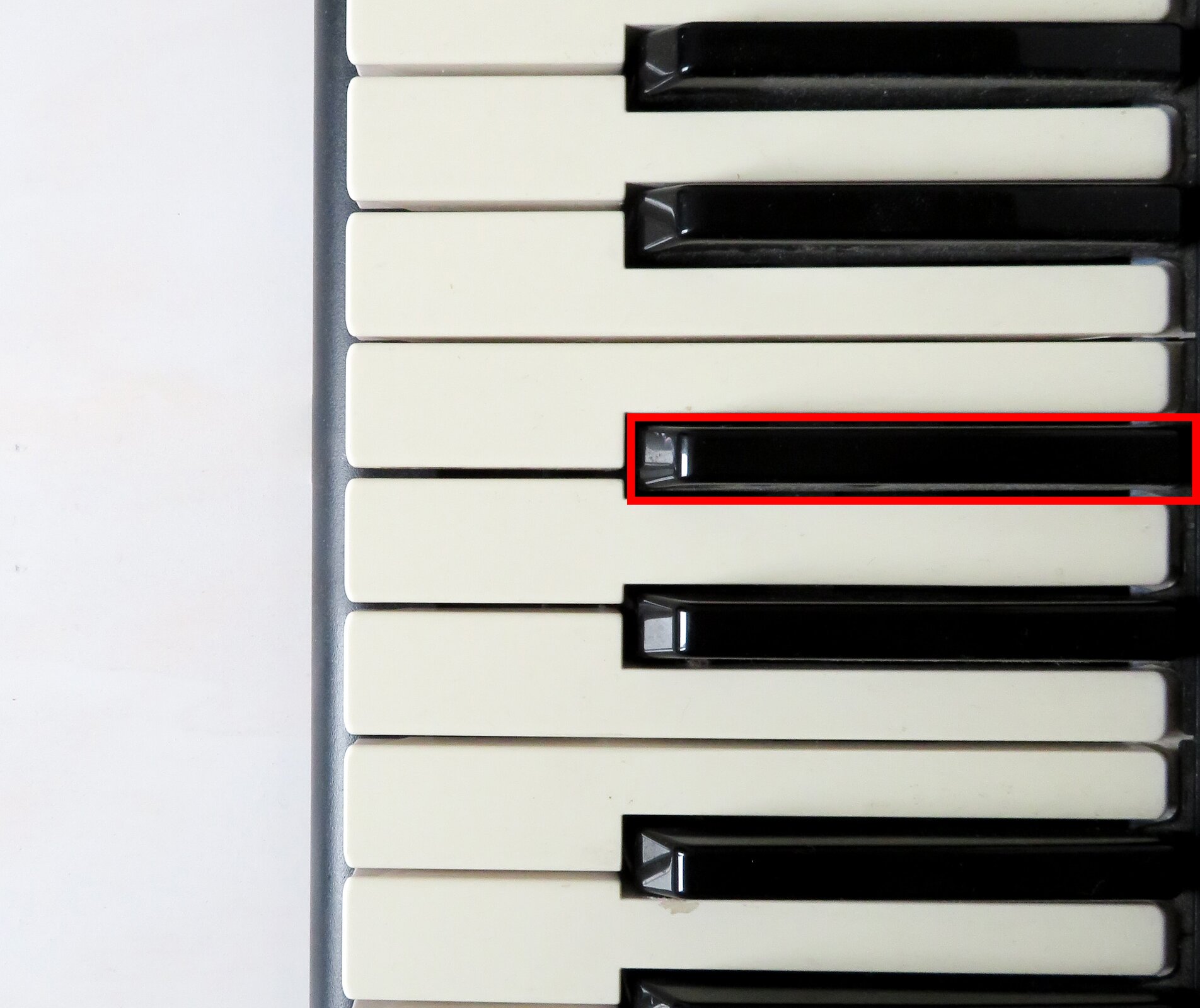 Zdjęcie przedstawia klawiaturę pianina z klawiszami białymi i czarnymi. Czerwona obwódka wskazuje na klawisz czarny.