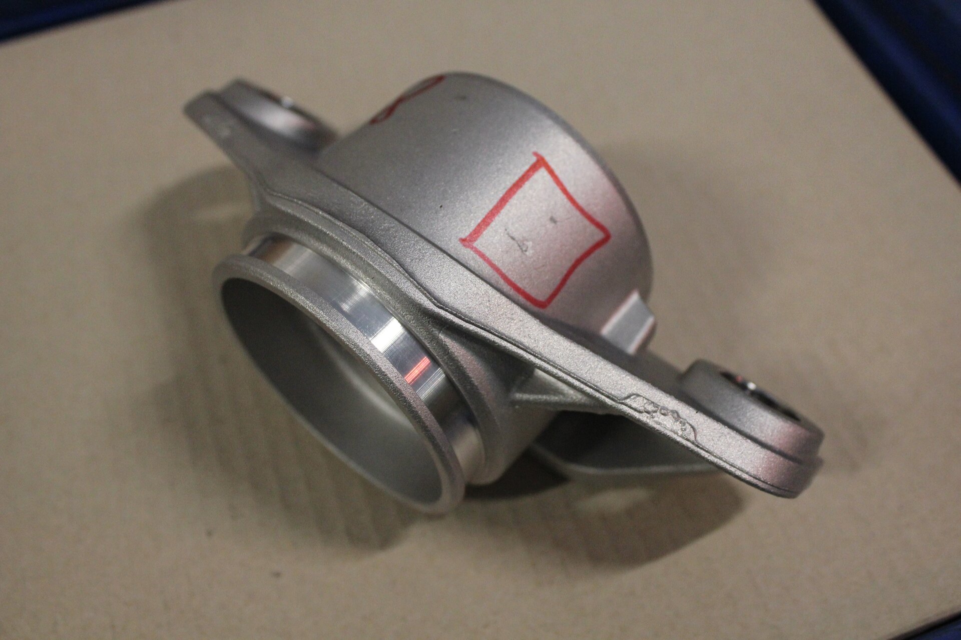 Ilustracja przedstawia odlew z wadą powierzchniową. Jest to srebrzysty element z wyszlifowaną tuleją. Na matowym korpusie, widoczne są wgłębienia.