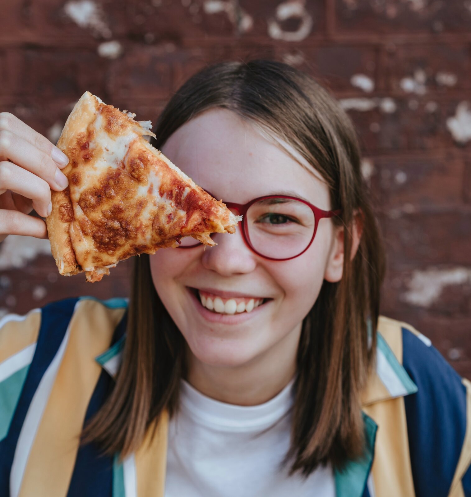 Na ilustracji  znajduje się dziewczynka trzymająca przed twarzą kawałek pizzy.