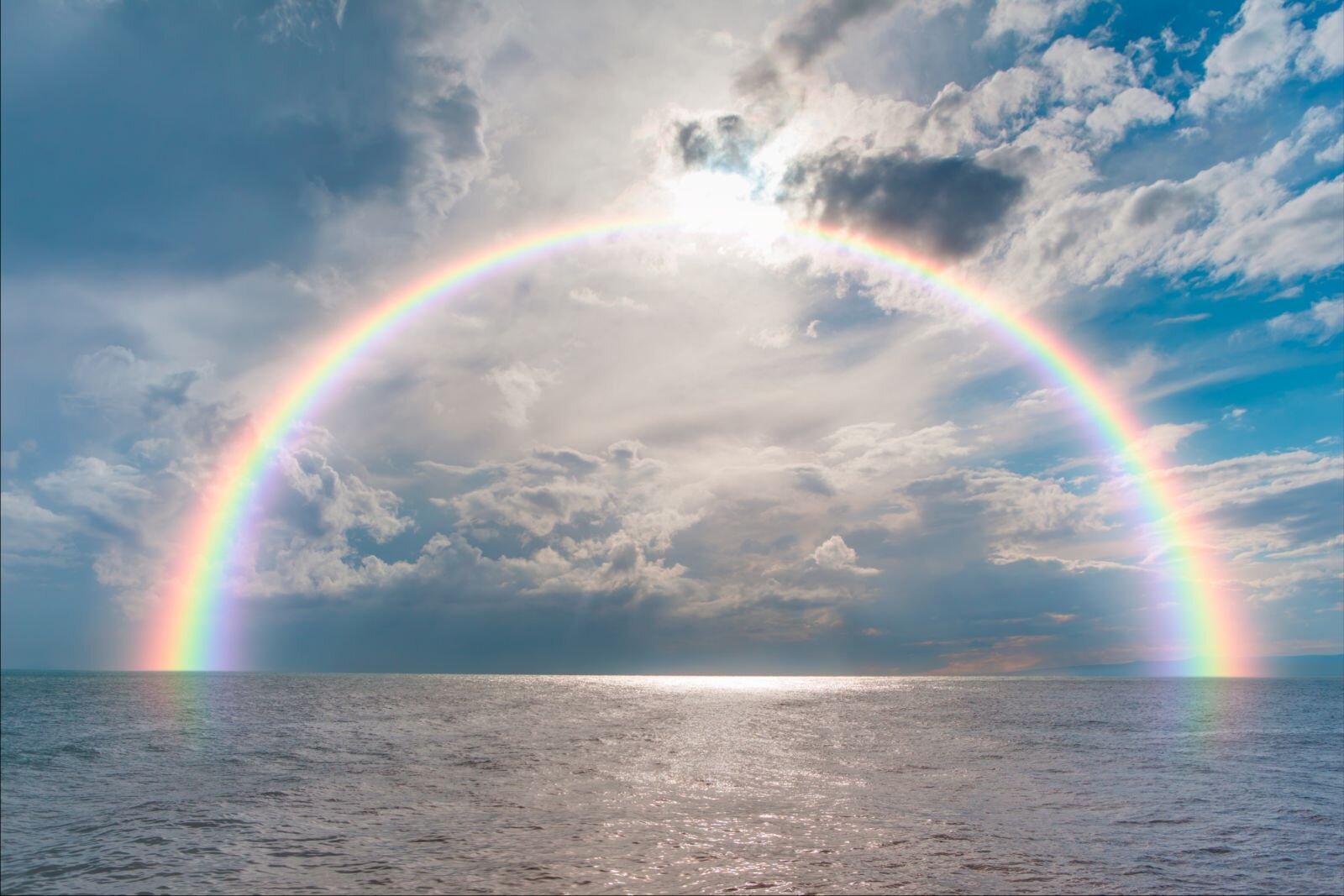 Zdjęcie przedstawia zjawisko atmosferyczne - tęczę, które powstaje na niebie pod wpływem rozszczepienia światła słonecznego przez krople deszczu. Kadr zajmuje morze i pogodne niebo, na którym w formie wielkiego łuku rozpościera się tęcza. Tęcza jest 7‑barwnym pasmem kolorów, ustawionych w określone kolejności.