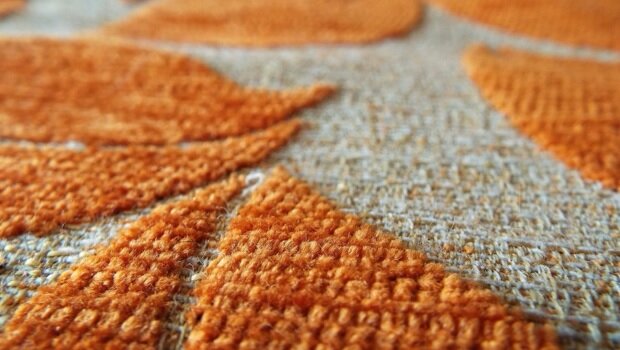 Zdjęcie przedstawia zbliżenie na beżowy sumak z pomarańczowym wzorem, układającym się w kształty liści.
