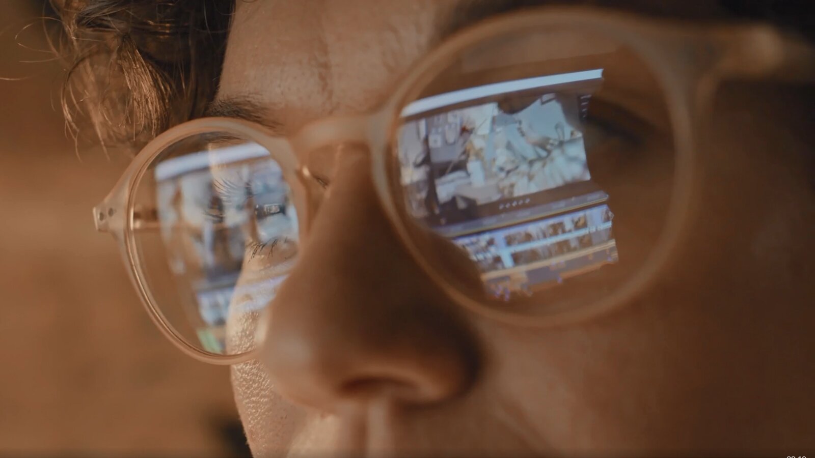 Zdjęcie przedstawia skupioną na pracy kobietę w okularach. W szkłach okularów odbija się monitor komputera.