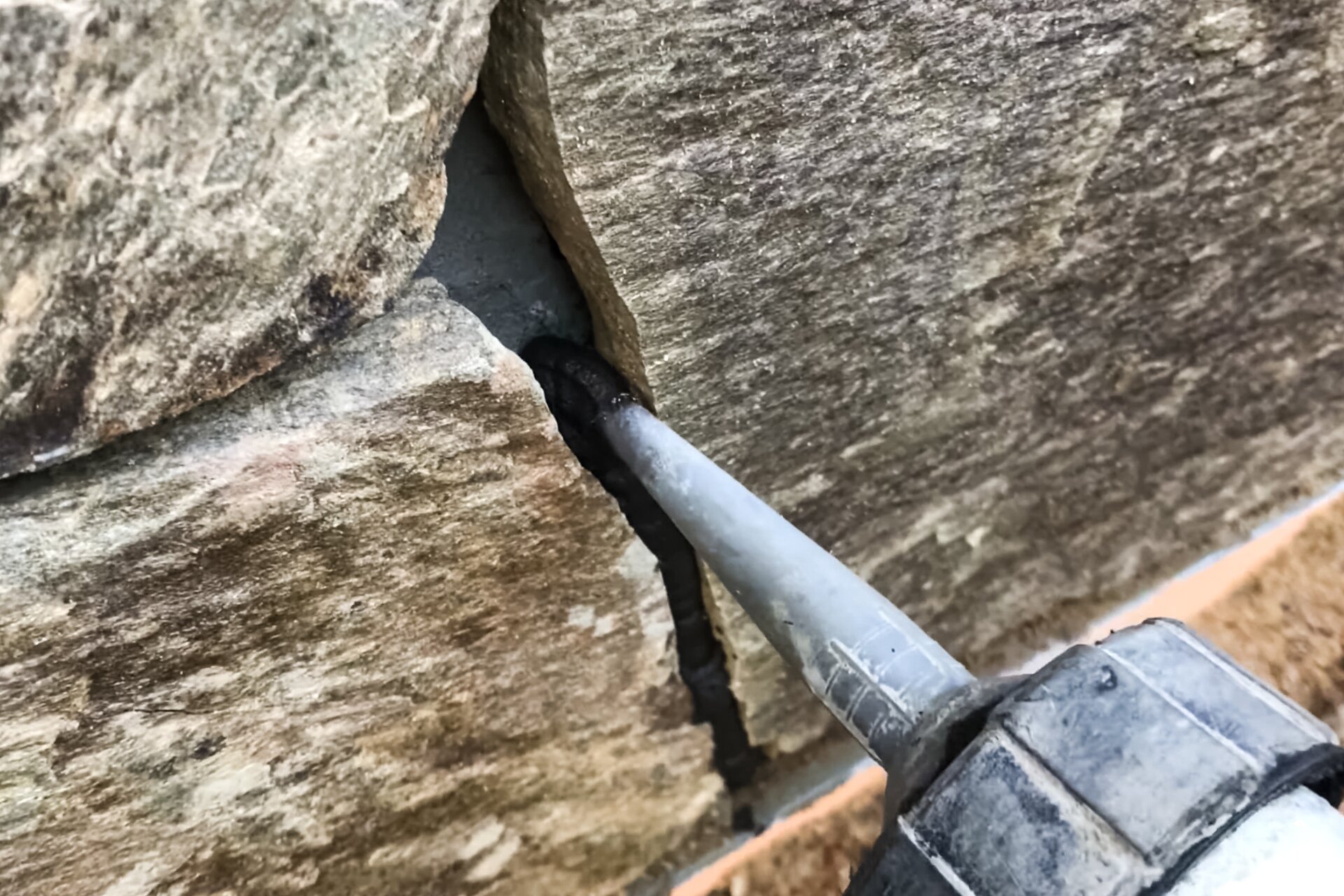 Zdjęcie przedstawia aplikację kremu hydrofobizującego podczas osuszania murów metodą iniekcji bezciśnieniowej. Widać końcówkę urządzenia nakładającą krem pomiędzy szpary w murze.