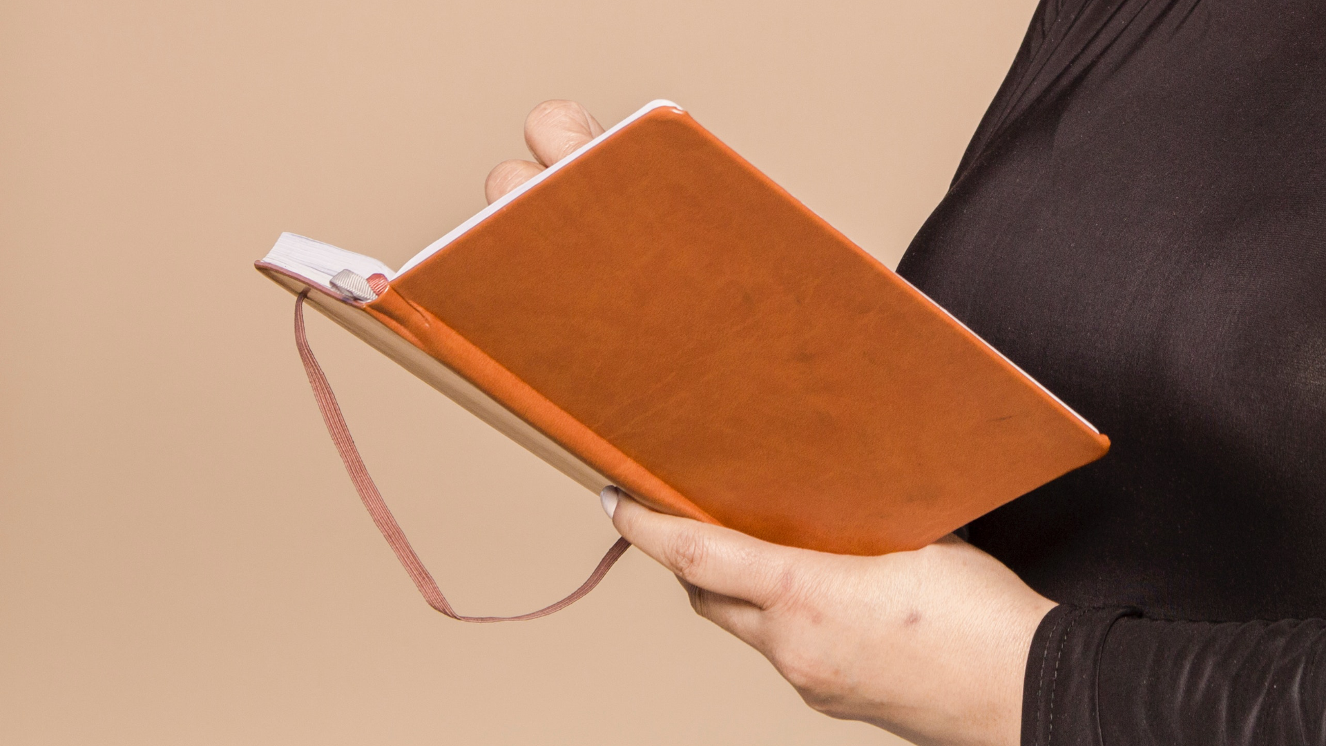 Zdjęcie przedstawia otwarty notes, który trzyma w rękach kobieta. Twarz kobiety pozostaje poza kadrem.