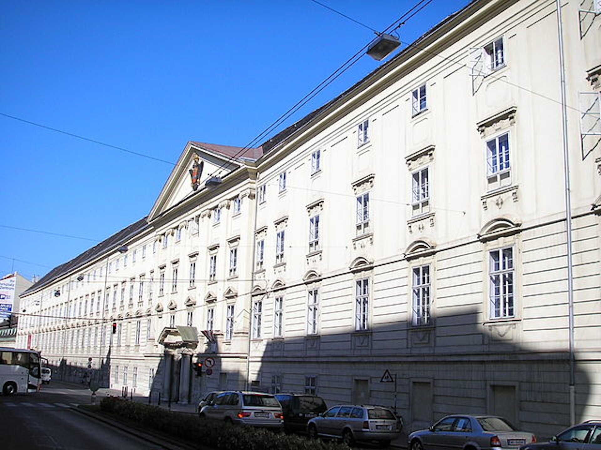 Rys. 1. Zdjęcie przedstawia piękny, duży, trzypiętrowy budynek. Jego elewacja jest jasna, budynek jest bardzo długi z rzędami ozdobnych okien. Dach ma spadzisty. Przed budynkiem widać ulicę z samochodami.