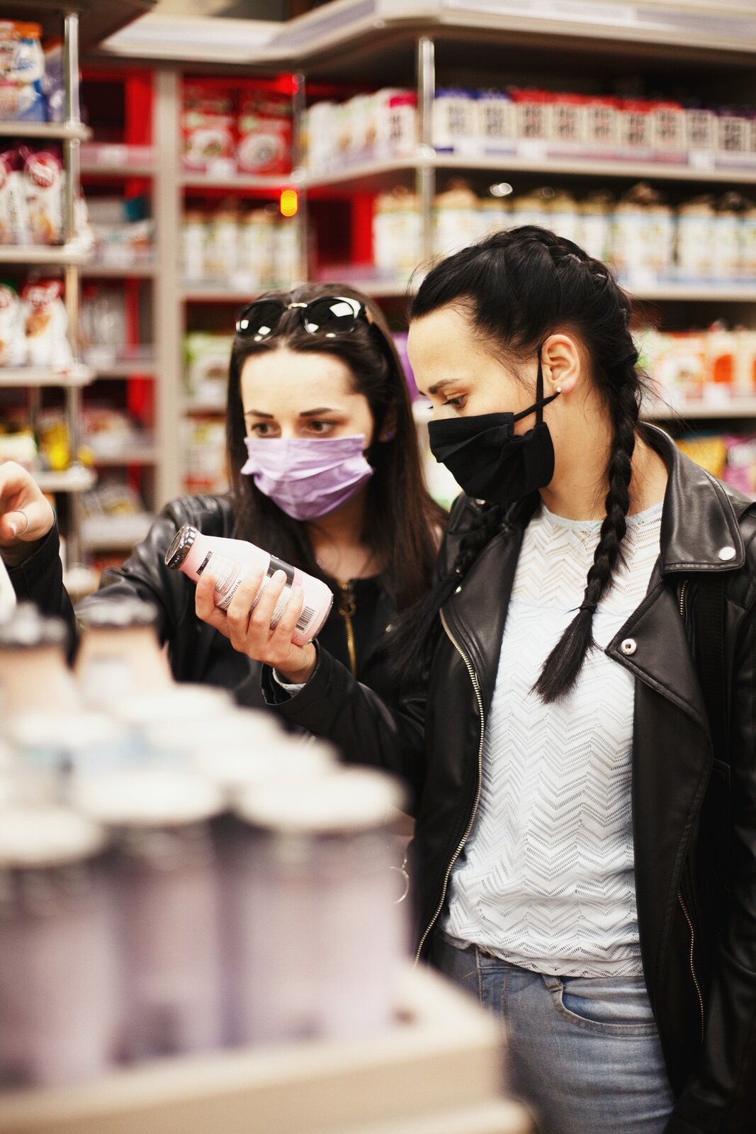 Zdjęcie przedstawia dwie młode dziewczyny uważnie przyglądające się produktom mlecznym w supermarkecie. W tle widać regały sklepowe pełne różnych produktów.