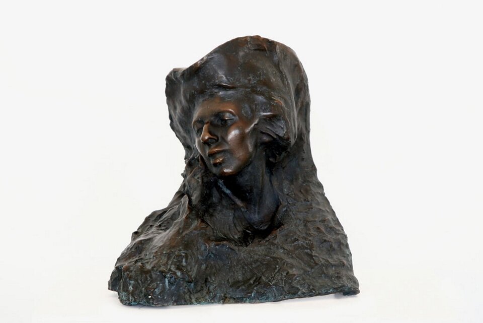 Ilustracja przedstawia rzeźbę pt. „Portret żony” autorstwa Stanisława Kazimierza Ostrowskiego. Rzeźba ukazuje twarz kobiety z lekko otwartymi ustami i przechyloną głową.