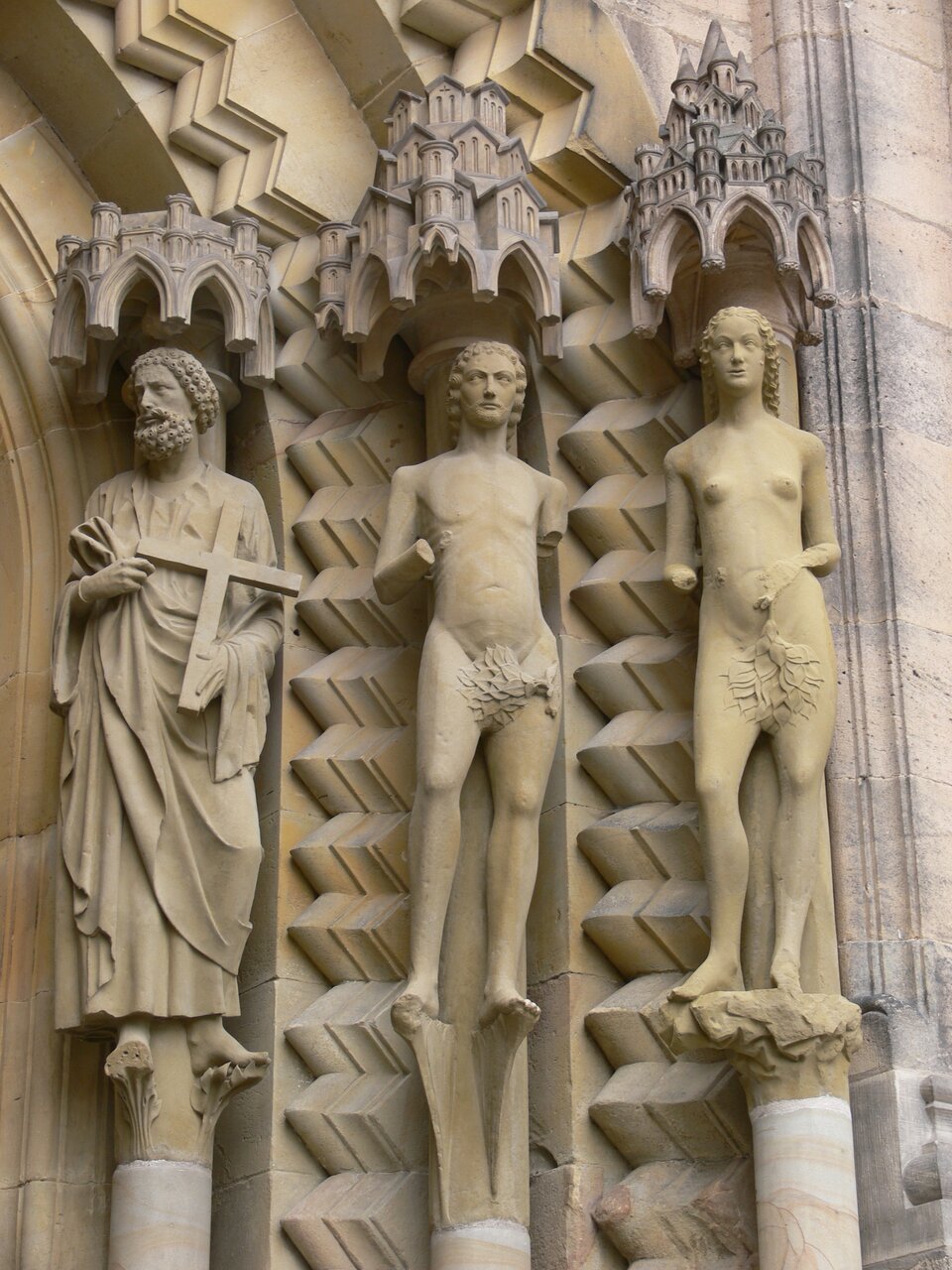 Ilustracja przedstawia posągi Adama, Ewy i św. Piotra, znajdujące się po prawej stronie ościeży portalu książęcego katedry w Bambergu. Rzeźby ustawione są na głowicach kolumn. Po lewej stronie stoi Piotr z krzyżem. Następnie Adam i Ewa, ukazani w aktach z liściem zasłaniającym przyrodzenie. Nad głowami figur znajdują się baldachimy w postaci budowli. 