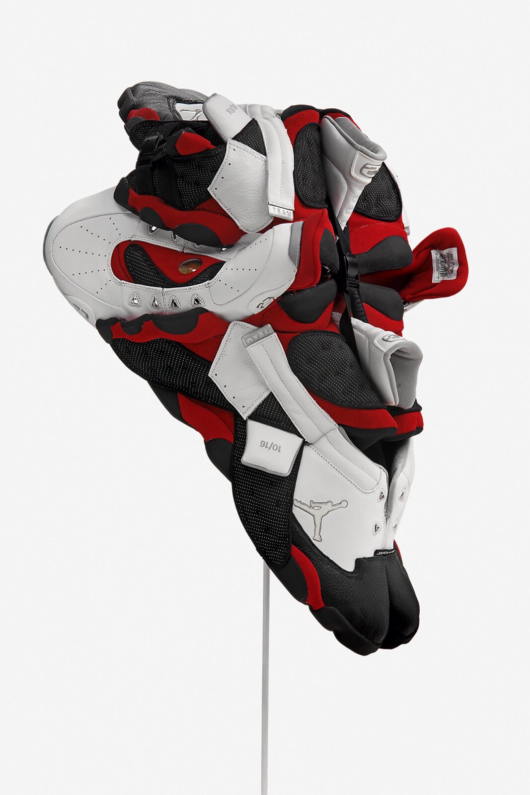 Dzieło przedstawione na fotografii wykonano z materiału obuwia sportowego. Rzeźba została sfotografowana z profilu. Logo produktu (z którego została stworzona rzeźba) widoczna jest u dołu - mężczyzna wyskakujący z piłką koszykową. Całość kształtem przypomina trójkąt, jednak jego strukturę przerywa kilka wystających nieznacznie elementów - głównie języków obuwia (znajdujące się u góry i po środku rzeźby) i ochraniaczy kostek (prostokątne białe elementy na rzeźbie znajdujące się u góry), ochraniaczy pięt i ścięgna achillesa (te elementy znajdują się po bokach pracy). Kolorystyka to czerń, biel oraz czerwień. Części, które najbardziej się wyróżniają to białe logo, biało‑czarna metka na czerwonym materiale oraz przód obuwia wraz ze srebrnymi otworami na sznurowadła. Dzieło przedstawia różne struktury elementów, pokazane jest na podwyższeniu - cienkiej szarej rurce.
