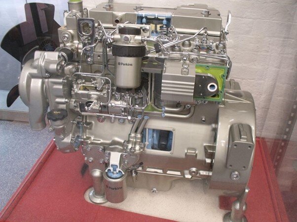 Grafika przedstawia silnik spalinowy umieszczony w gablocie. Silnik ma zwartą budowę, składa się z licznych połączonych ze sobą części. 