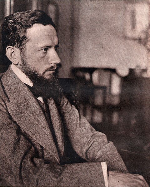 Zdjęcie przedstawia prawy profil siedzącego mężczyzny. To człowiek w dojrzałym wieku. Ma gładko zaczesane, krótkie włosy i gęstą brodę. Ubrany jest w surdut. 