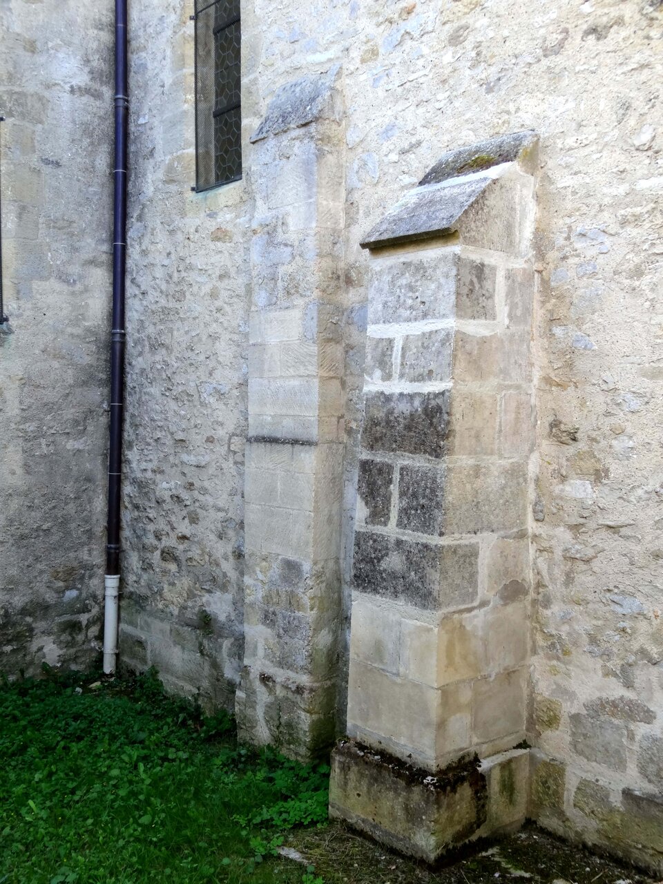 Ilustracja o kształcie pionowego prostokąta zbliżonego do kwadratu przedstawia fotografię fragmentu ściany romańskiego kościoła. Ściana wykonana jest z kamienia. Po lewej znajduje się fragment rynny oraz wąskiego okna. Po lewej do ściany przylegają dwie przypory: lewa wyższa, prawa niższa. Obie zostały wykonane z ciosów kamiennych.  
