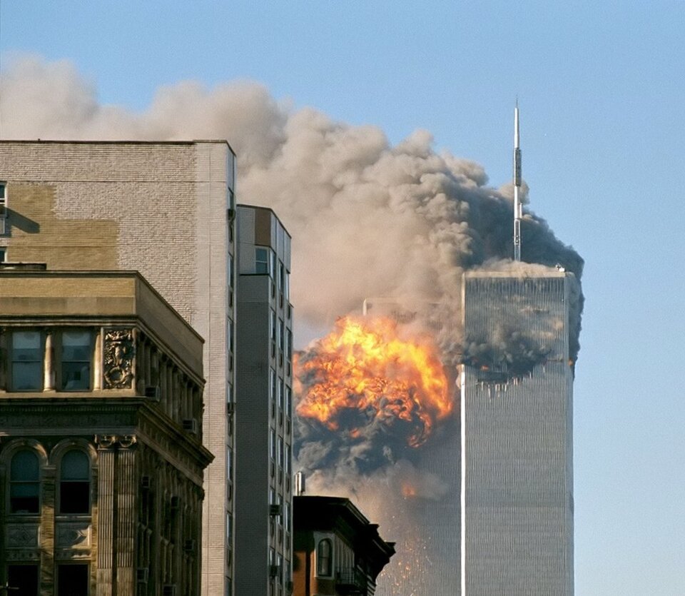 Zdjęcie przedstawia płonące wieże World Trade Center. Płoną dwa wysokie wieżowce. Unosi się bardzo gęsty, szary dym.
