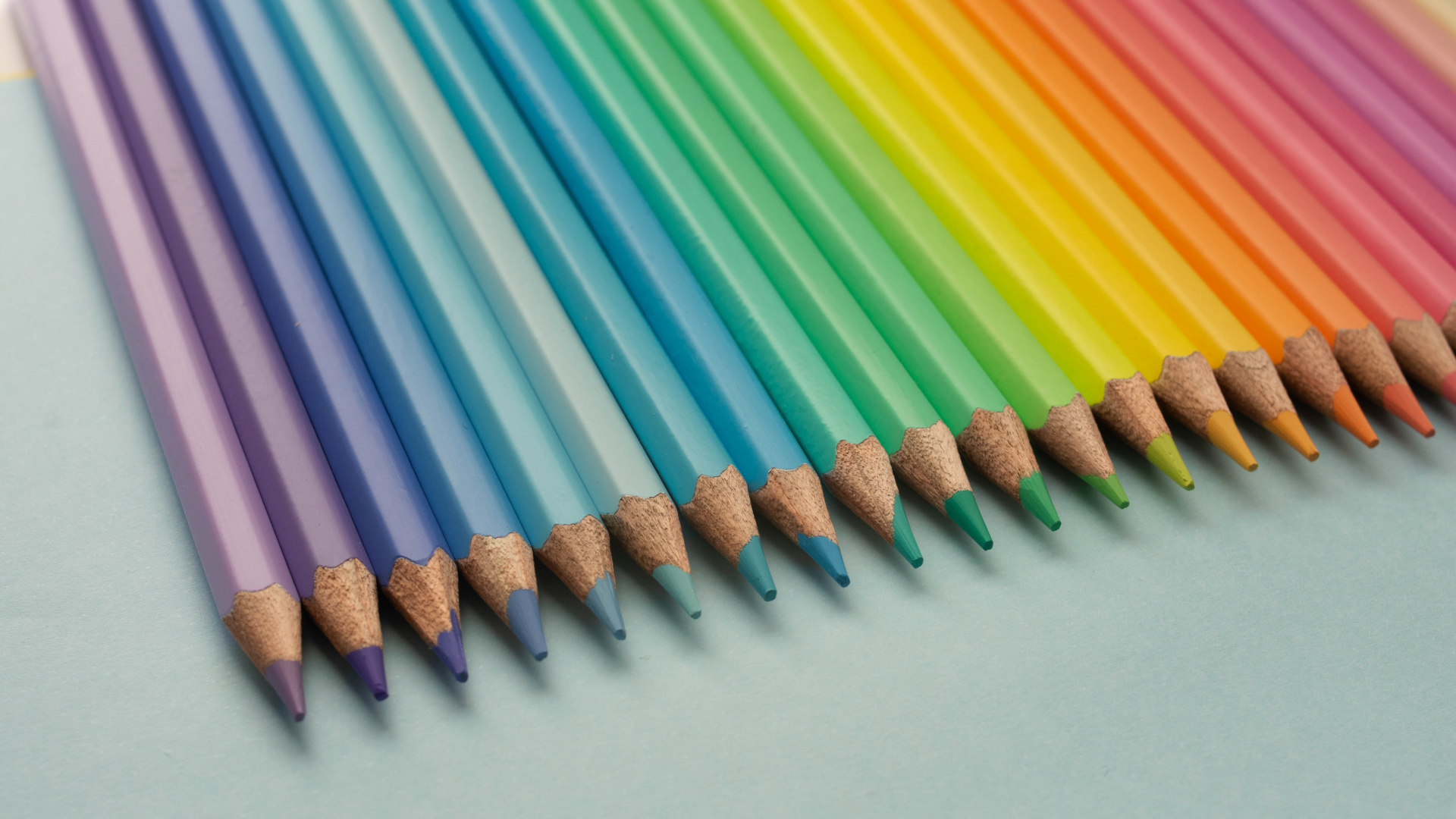 Zdjęcie przedstawia kolorowe kredki ołówkowe. Kredki ułożone są równo jedna przy drugiej. Razem, kolorystycznie tworzą wzór tęczy.