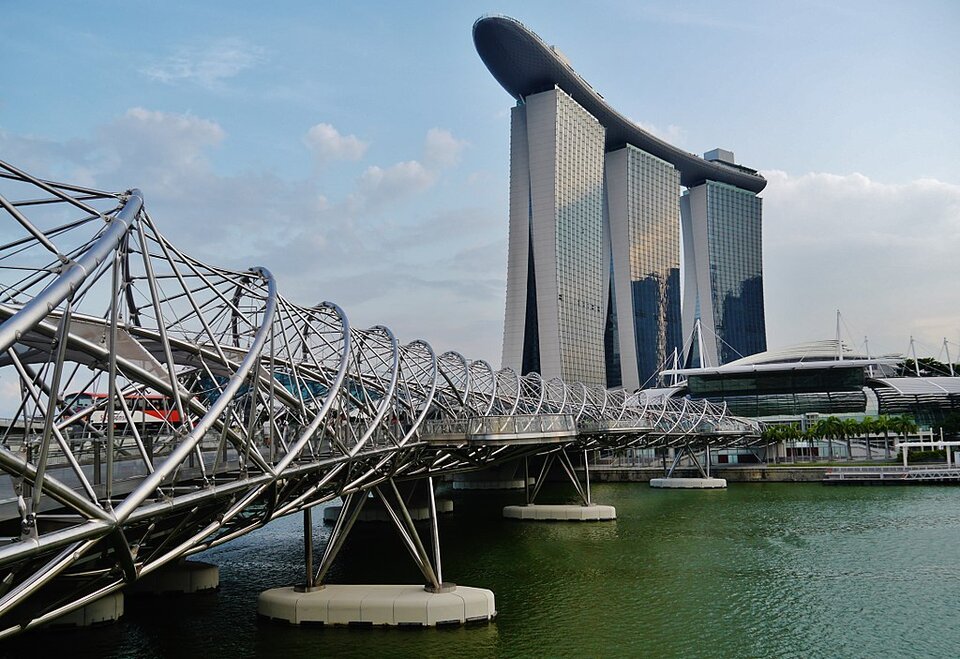 Zdjęcie przedstawia Helix Bridge – kładkę dla pieszych nad zatoką Marina Bay w Singapurze w kształcie spirali ze srebrnych, skręconych rurek. W tle znajduje się Marina Bay Sands  - hotel składający się z 3 wysokich wieżowców połączonych na górze Sky Parkiem w kształcie łodzi.