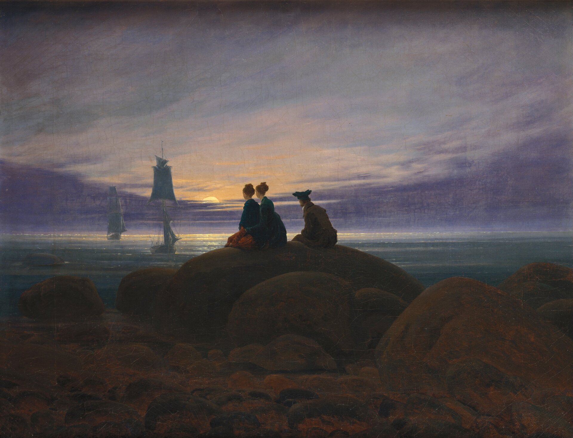 Obraz przedstawia krajobraz nadmorski. Na ogromnych kamieniach spoczywających na piaszczystej plaży siedzą dwie kobiety w długich sukniach i mężczyzna w marynarce, spodniach i kapeluszu. Siedzący obserwują morze, po którym płyną spokojnie dwa żaglowce. Zachodzi słońce.