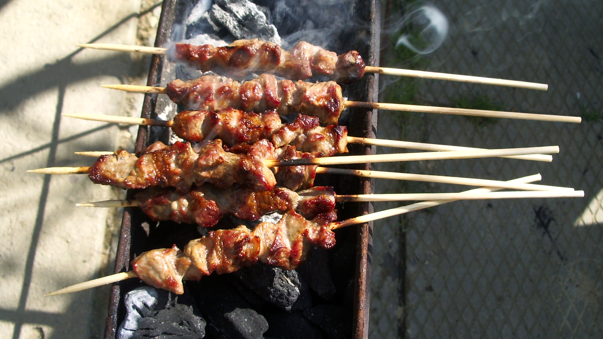 Zdjęcie przedstawia arrosticini - mięsne szaszłyki na patykach, które leżą nad rozgrzanym węglem.