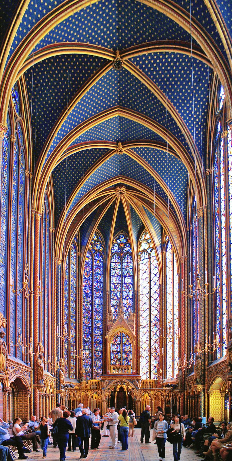 Ilustracja o kształcie pionowego prostokąta przedstawia wnętrze górnej kaplicy w Saint Chapelle. Na ilustracji widoczna jest bogato zdobiona polichromia sklepienia, dekorowanego gwiazdami na niebieskim tle. Ściany wypełnione są smukłymi, ostro zakończonymi oknami witrażowymi. Wewnątrz znajdują się wierni.  