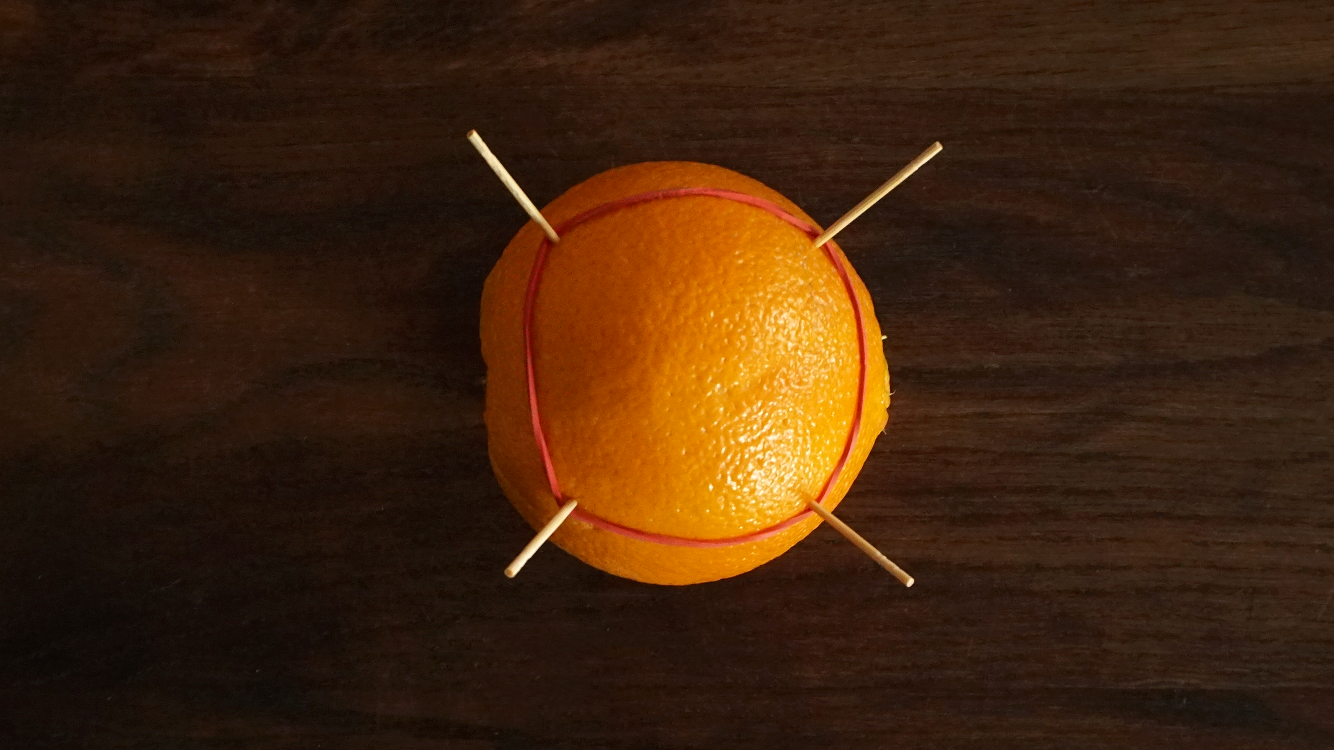 Zdjęcie przedstawia pomarańczę, w którą wbito cztery zapałki. Na zapałki założono gumkę recepturkę, która utworzyła czworokąt, którego kąty wewnętrzne są rozwarte.