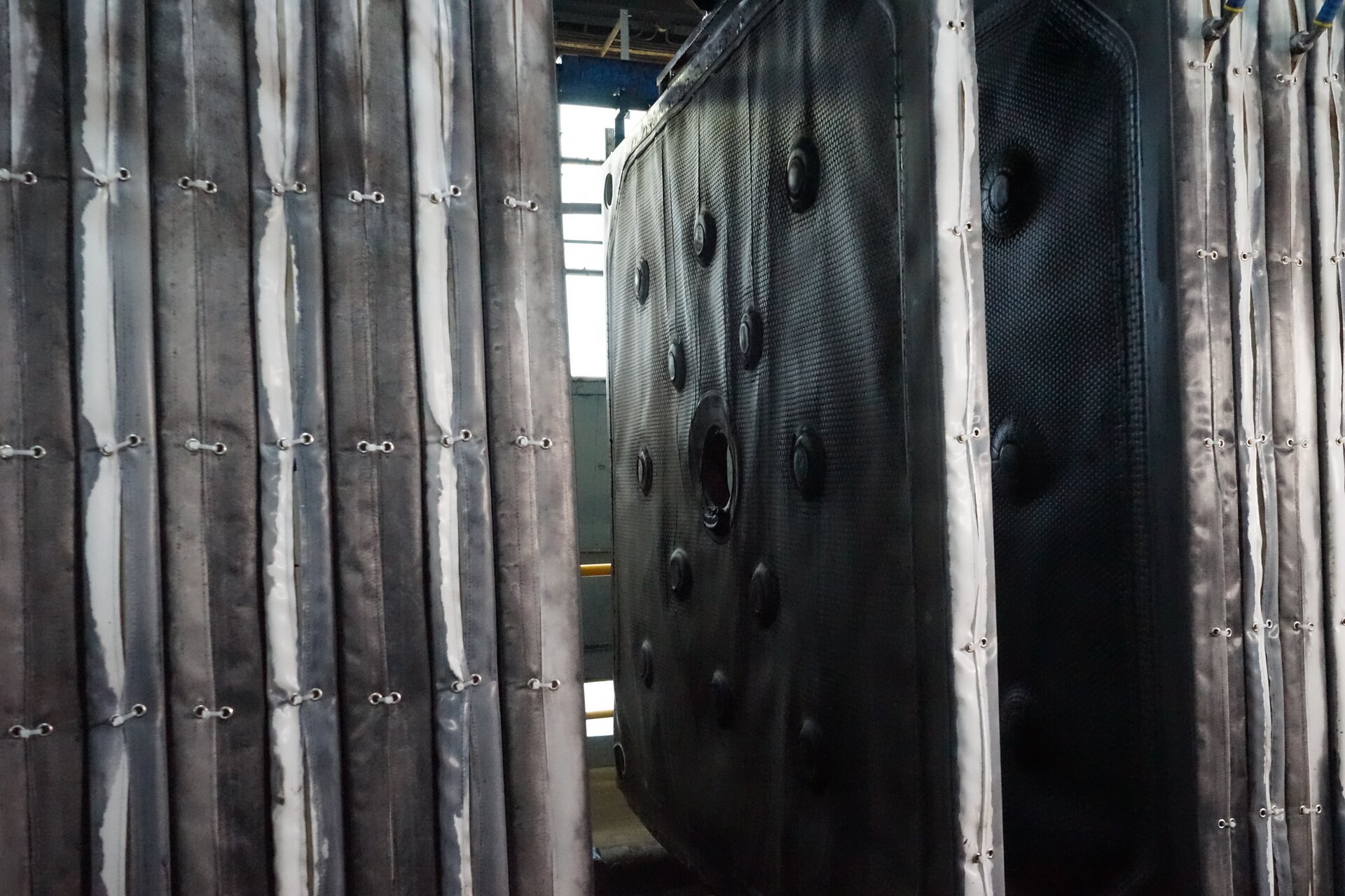 Ba zdjęciu widoczne są filtry prasy filtracyjnej. Filtry są w kształcie cienkich prostopadłościanów. Filtry widoczne z lewej strony zdjęcia rozmieszczone są obok siebie. Pomiędzy filtrami znajdującymi się z prawej strony widoczna jest przerwa. Materiał filtrów jest czarny i mokry. W centralnej części filtra znajduje się otwór. Wokół otworu rozmieszczonych jest dwanaście okrągłych elementów. Elementy są wypukłe.