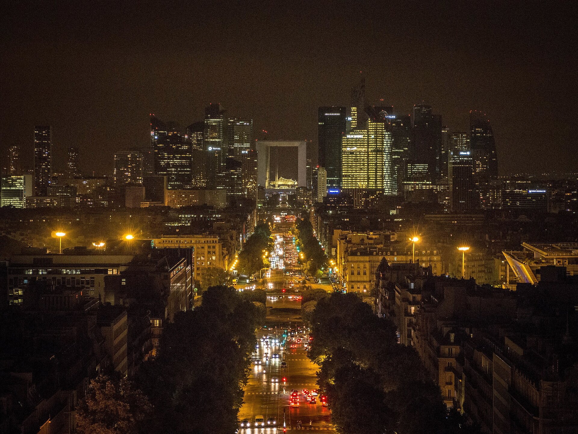 Na zdjęciu widok na biurowe wieżowce nocą. Pośrodku szeroka, oświetlona aleja z samochodami.