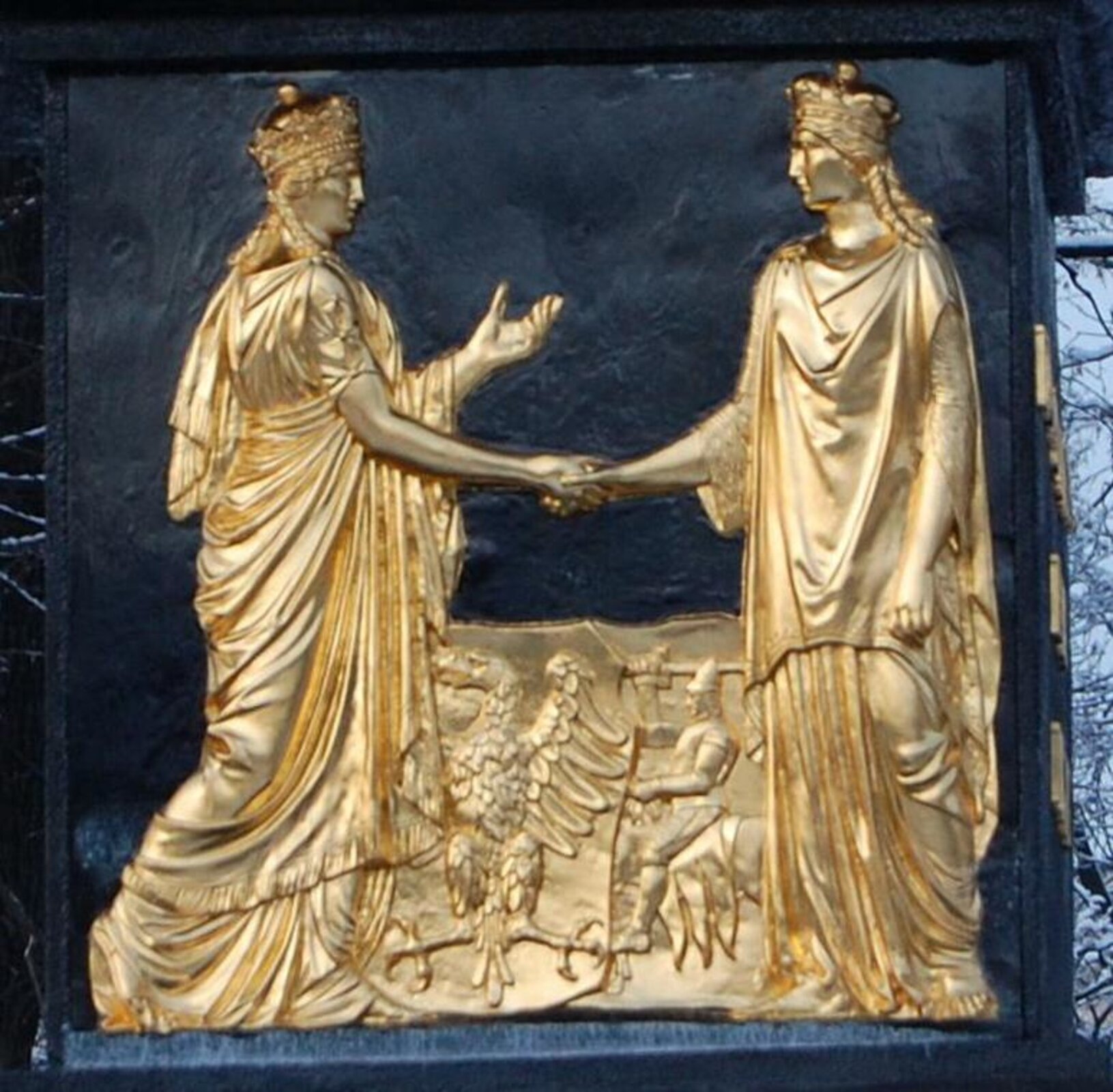 Fotografia barwna przedstawiająca płaskorzeźbę będącą częścią pomnika Związku Lubelskiego w Lublinie. Na płaskorzeźbie dwie postaci kobiece symbolizujące Polskę i Litwę podają sobie ręce, w tle herby obu państw.