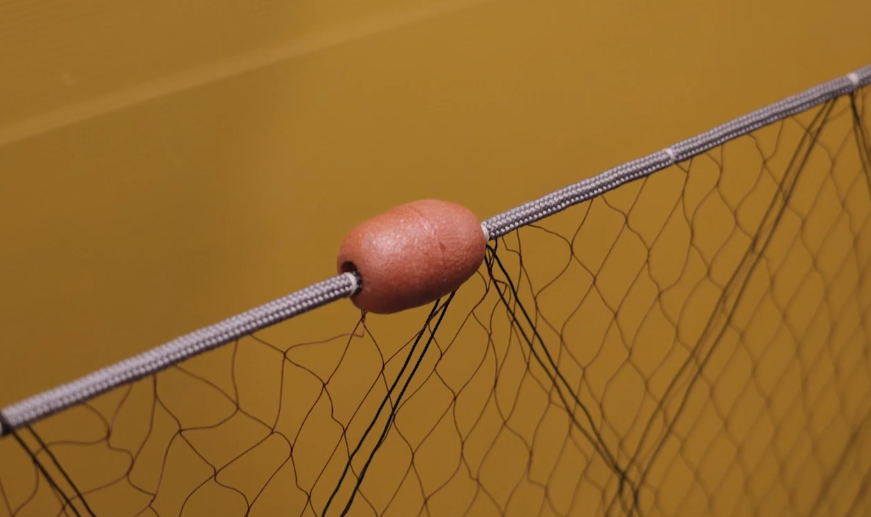 Na zdjęciu widoczny jest przykładowy pływak. Jest to walcowata bojka, zamocowana do górnej liny sieci rybackiej. Jej zadaniem jest utrzymywanie sieci w pozycji pionowej.