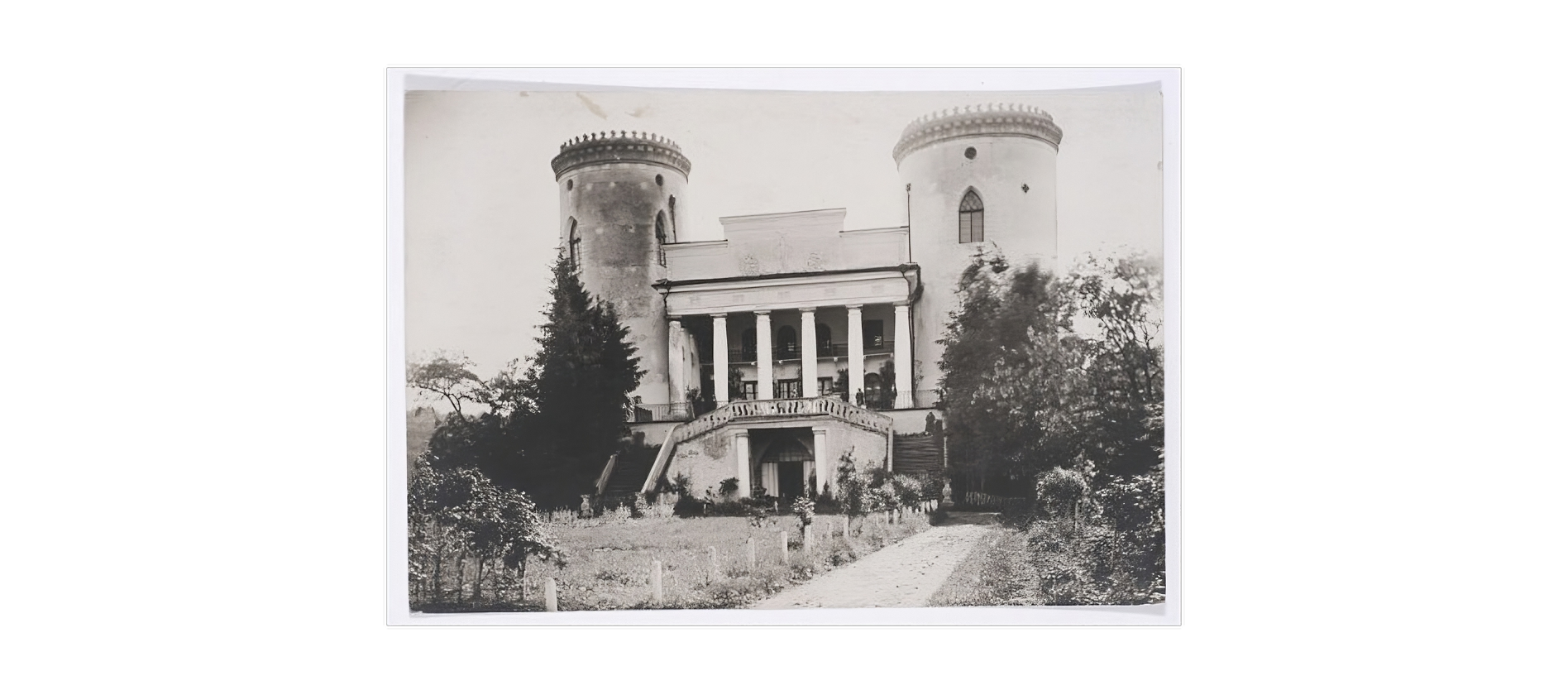 Zdjęcie przedstawia wygląd barokowego pałacu autorstwa Pierre’a Ricauda de Tirregaille'a [czyt.: piere rikode du tirugajła] na początku XX wieku. Pomiędzy dwoma okrągłymi wieżami dawnego założenia bastionowego znajduje się przebudowany od strony ogrodu w stylu klasycystycznym gmach główny. Wejście na werandę tarasową ocienia sześciokolumnowy portyk na poziomie pierwszego piętra. Od niego spływają w dół dwubiegowe schody. Poniżej nich znajduje się na parterze wejście do pałacu między dwoma kolumienkami. Lewą wieżę oplata bluszcz do poziomu okien na trzeciej kondygnacji budynku. Przed pałacem znajduje się trawnik z krzewami, rabaty kwiatowe i alejka spacerowa. 