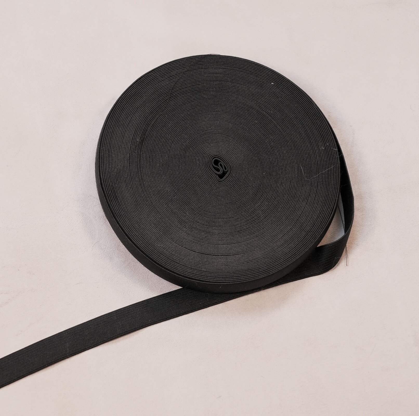 Zdjęcie przedstawia rolkę częściowo rozwiniętej, czarnej taśmy. 