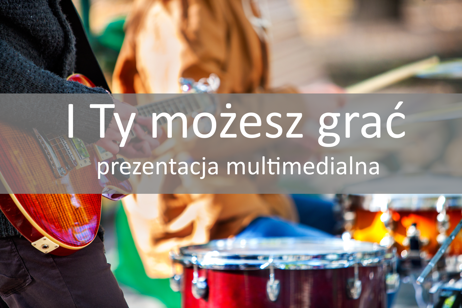 Fotografia przedstawia fragment tułowia muzyka, który gra na gitarze w pozycji stojącej. Osoba ubrana jest w ciemny sweter, palcami wydobywa dźwięk ze strun gitary. W tle perkusista ubrany w brązową kurtkę. Na fotografii umieszczono szare tło z białym napisem: I Ty możesz grać. Prezentacja multimedialna.