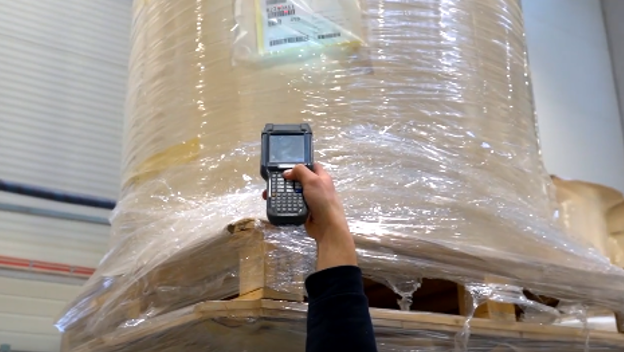 Grafika przedstawia czytnik etykiet logistycznych. W górnej części skanera znajduje się świecąca się na czerwono dioda laserowa. Obok skanera znajduje się kod kreskowy.