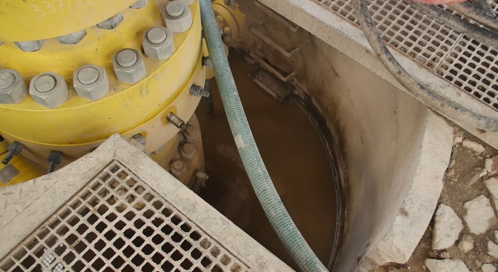 Na zdjęciu widoczna jest więźba rurowa z góry. Więźby rurowe służą do podwieszania rur okładzinowych zapuszczonych i zacementowanych w otworze wiertniczym oraz do instalowania na nich głowic przeciwerupcyjnych. Po zakończeniu wiercenia, gdy otwór przekazywany jest do eksploatacji, na więźbie montuje się głowicę eksploatacyjną. Na zdjęciu widoczny jest otwór. W jego środku znajduje się więźba, a na niej zamontowana jest głowica. W otworze znajduje się płyn. Obok głowicy widoczne są różne przewody.Poniżej zdjęcia w prawym dolnym rogu widoczny jest przycisk odtwarzania. Tekst nagrania jest zgodny z tytułem zdjęcia.