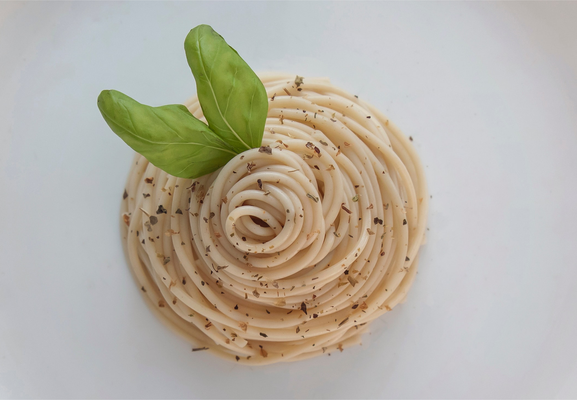 Zdjęcie przedstawia danie z makaronem ułożone w kółko na talerzu. Danie przybrane jest dwoma listkami bazylii.