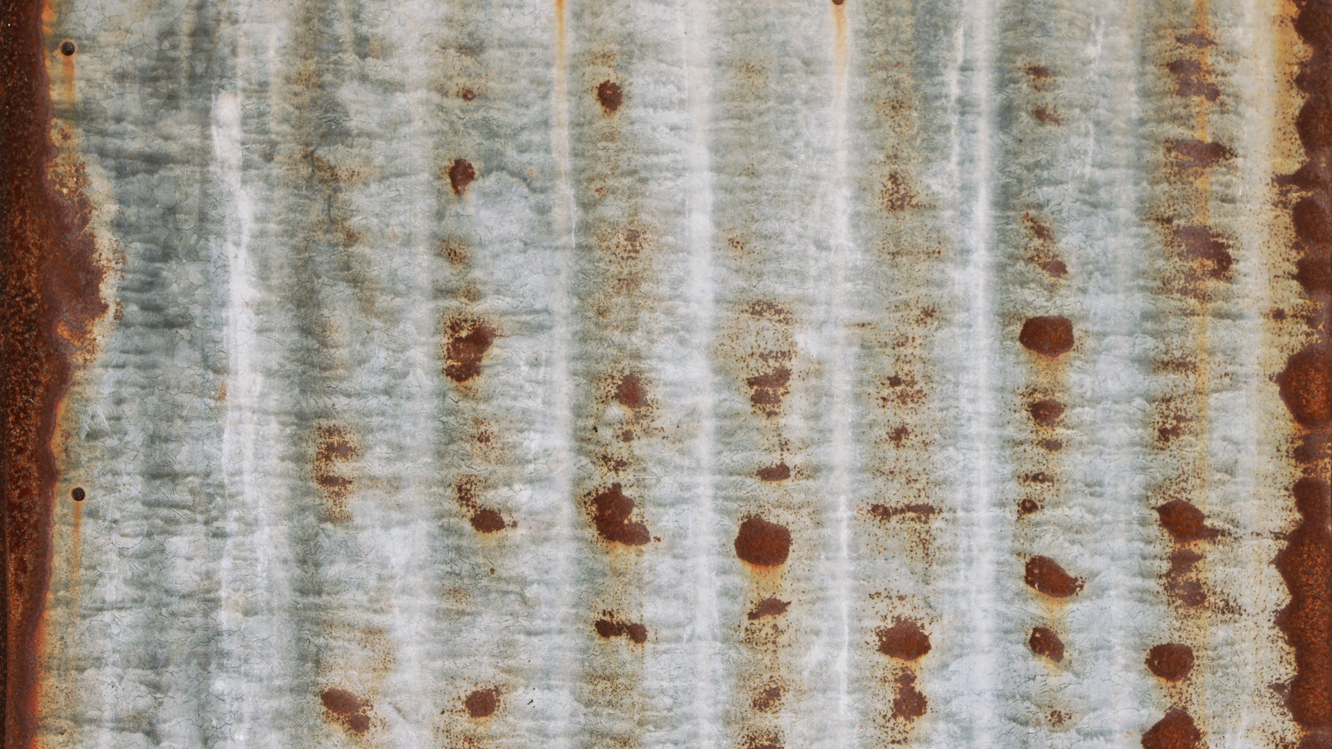 Zdjęcie przedstawia kawałek skorodowanej blachy pokrytej rdzą.