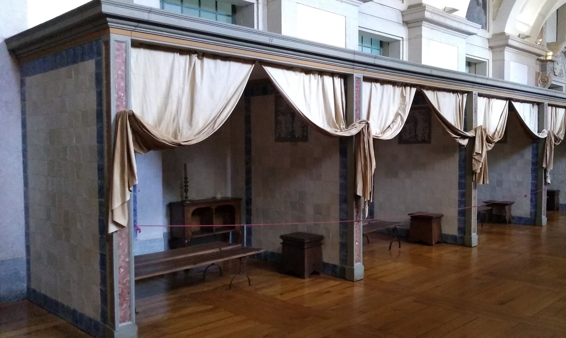 Zdjęcie przedstawia wydzielone małe pomieszczenia z ławami i szafkami. Przy wejściach do nich znajdują się zasłony.