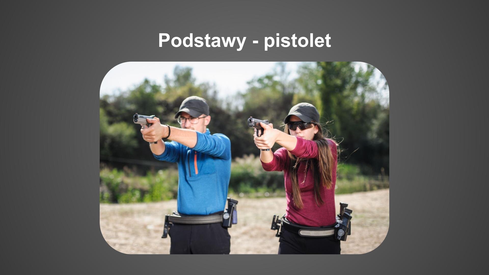 Szara plansza. U góry biały napis: „Podstawy - pistolet”. Poniżej zdjęcie przedstawiające parę osób strzelających z pistoletu. Mężczyzna, stojący z lewej strony, ubrany jest w ciemne spodnie, niebieską bluzę i szarą czapkę z daszkiem. Na biodrach ma pas z magazynkami. Obok niego, z prawej strony, stoi kobieta w długich, brązowych włosach. Ubrana jest w ciemne spodnie, bordową bluzę, ciemną czapkę z daszkiem i okulary przeciwsłoneczne. Do bioder, podobnie jak mężczyzna, ma przymocowany pas z magazynkami. Oboje prostują ręce i w obu dłoniach trzymają pistolety. W tle piaskowa droga i zielone drzewa oraz krzewy.