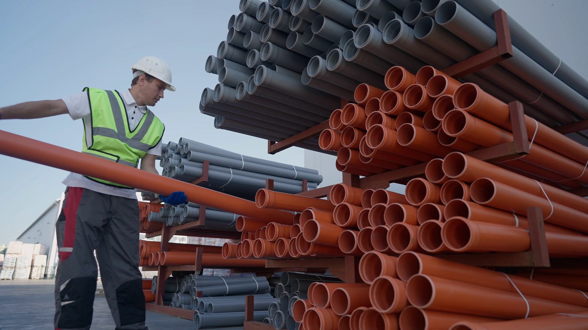 Na grafice przedstawiono, jak mężczyzna w stroju budowlanym umieszcza rurę na stosie rur. Rozmieszczenie rur: obejmuje przetransportowanie rur i ich rozładunek wzdłuż pasa montażowego.