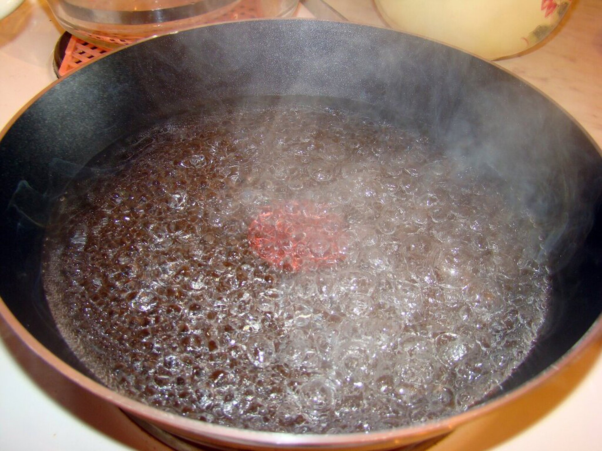 Rys. 2. Zdjęcie przedstawia gotującą się wodę w płaskim naczyniu. Powierzchnia wody jest pofalowana, nad nią unosi się para i pojawiają się liczne bąble powietrza. Woda jest w stanie wrzenia.