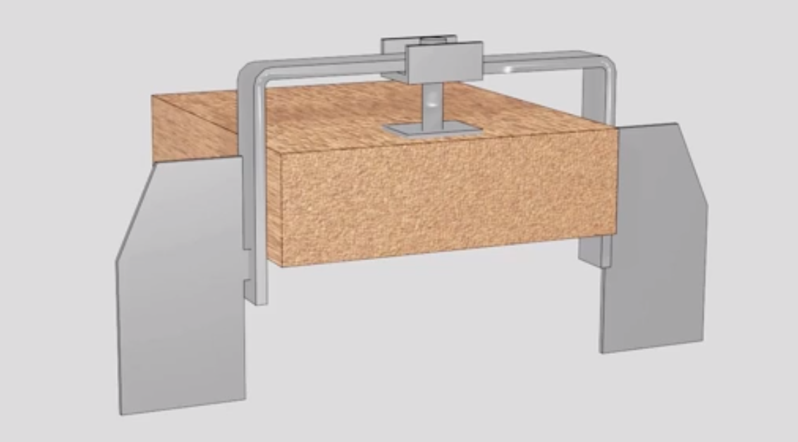 Ilustracja przedstawia opórkę przeciwpełzną. Na środku znajduje się prostopadłościenny kawałek drewnianego podkładu. Jest on utrzymywany w miejscu w metalowej ramce z dwoma płaskimi podpórkami po bokach.