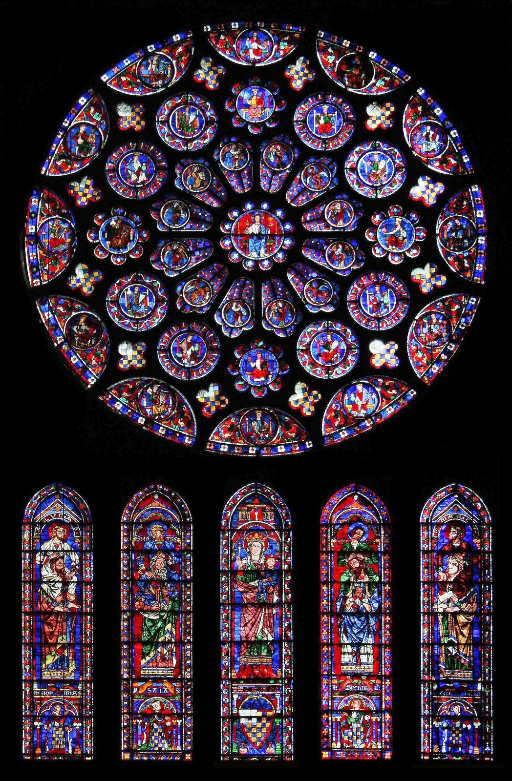 Zdjęcie przedstawia rozetę i pięć podłużnych okien z witrażami umieszczonymi poniżej rozety w Katedrze Chartres. W centralnej części rozety znajduje się Jezus Chrystus. Poniżej rozety znajdują się cztery smukłe witraże zakończone łukiem ostrym.