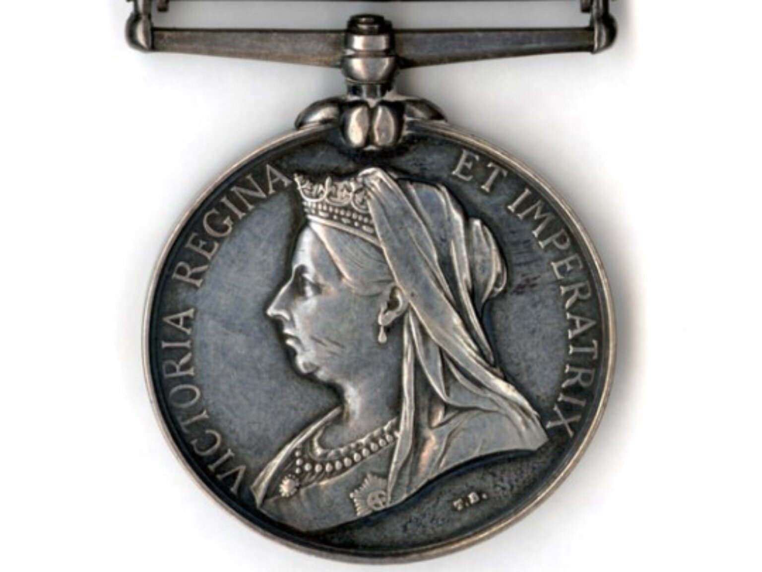 Zdjęcie przedstawia jubileuszowy medalion z popiersiem królowej Wiktorii z lewego profilu. Królowa ma na głowie koronę z welonem, kolczyki w uszach i głęboki dekolt sukni, na którym widać kolię. Wokół widoczny jest napis w języku łacińskim: VICTORIA REGINA ET IMPERATRIX. W górnej części medalionu widoczne jest ozdobne zapięcie. 