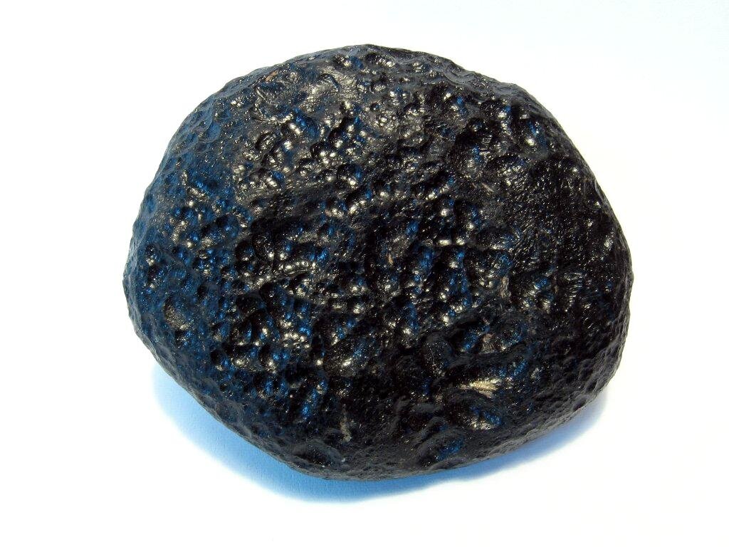 Na zdjęciu znajduje się okrągły kamień o chropowatej, ale połyskliwej powierzchni. Ma czarny kolor.